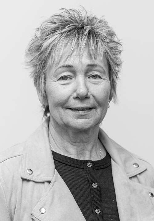 sandy-mitchell - Sellar & Sellar Portrait of an older woman with short gray hair, wearing a light jacket and dark top, smiling softly.